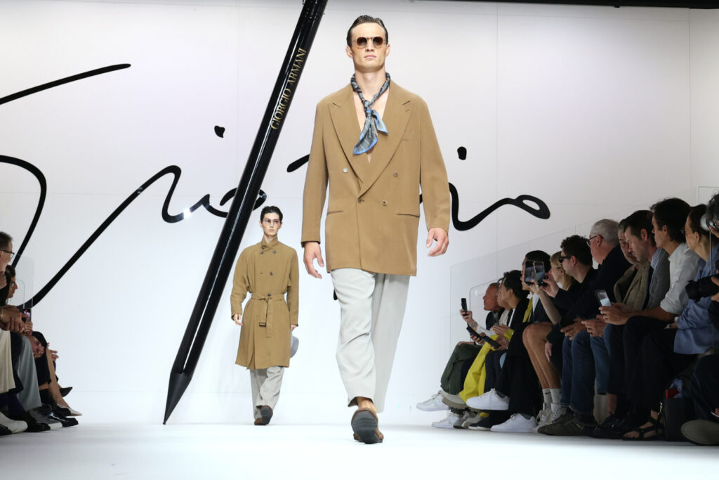 Ανδρική μόδα: τάσεις άνοιξη/καλοκαίρι 2024 από τις πασαρέλες – μοντέλο με καμηλό παλτό και φουλάρι στο λαιμό - Giorgio Armani