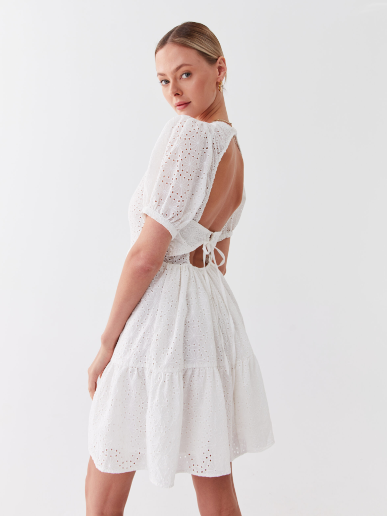 Μοντέλο με λευκό διάτρητο καλοκαιρινό φόρεμα με ανοιχτή πλάτη