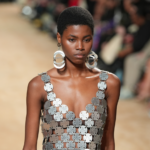 αξεσουάρ μόδας για το 2024 – γυναίκα με τεράστια ασημένια σκουλαρίκια και ασημένιο φόρεμα φτιαγμένο από συνδεδεμένες μεταλλικές πλάκες